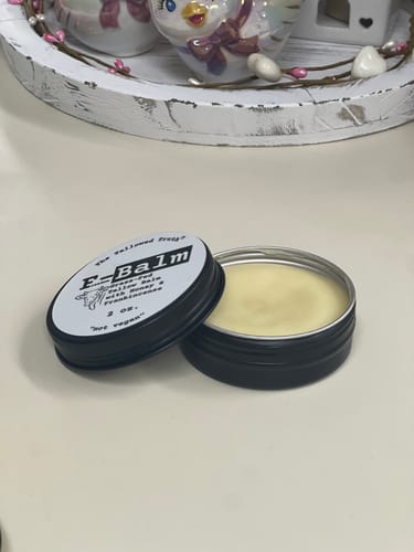 Customer's open black tin of F-Balm, with the lid beside it, showing the solid yellow balm.