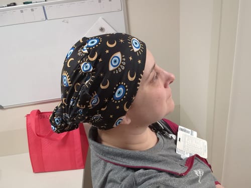 Customer in profile wearing the black DuoStyle Scrub Hat with the 'Evil Eye' pattern, gathered neatly at the back.