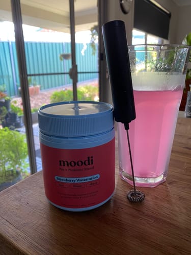 Reviewer's tub of Pre + Probiotic Blend with a frother and a glass of the prepared Pink Lemonade.