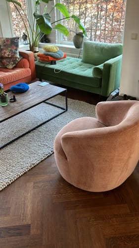 Recensent's Hug draaibare fauteuil in terra-kleur, schuin van achteren gezien in een woonkamer.