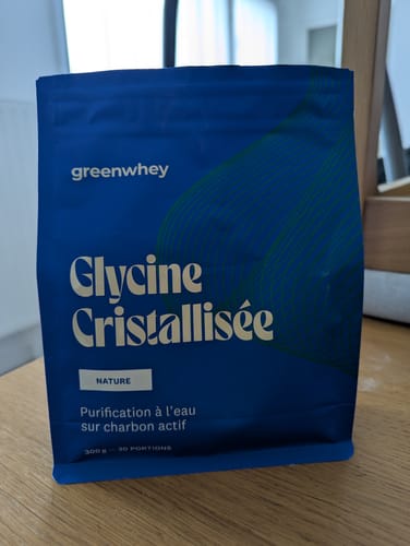 Un client montre le sachet bleu de Glycine Cristallisée posé sur une table en bois.