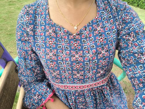Customer wearing the Golden Deer Heart Necklace outdoors with a blue patterned dress.