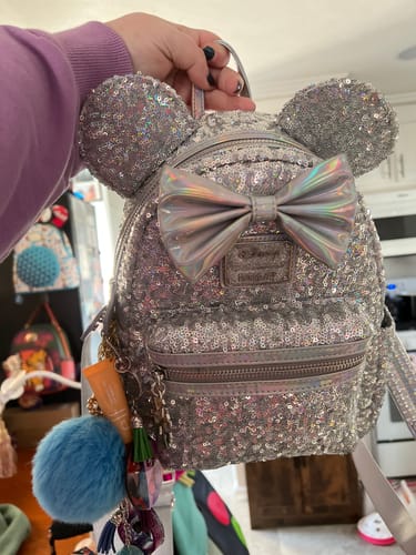 A reviewer holding up the Loungefly Disney Minnie Mouse backpack, showing its silver holographic sequins and bow.