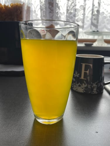 Reviewer's yellow energy drink served in a clear glass on a tabletop.