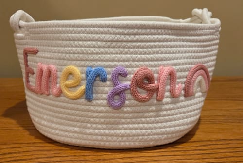 Customer's personalized knitted basket with 'Emerson' in multicolor yarn and a knitted rainbow icon.