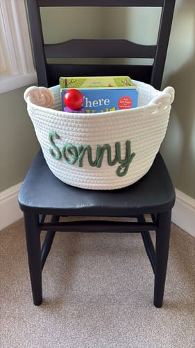 Customer's personalized knitted basket with 'Sonny' in green yarn, holding books and a toy.
