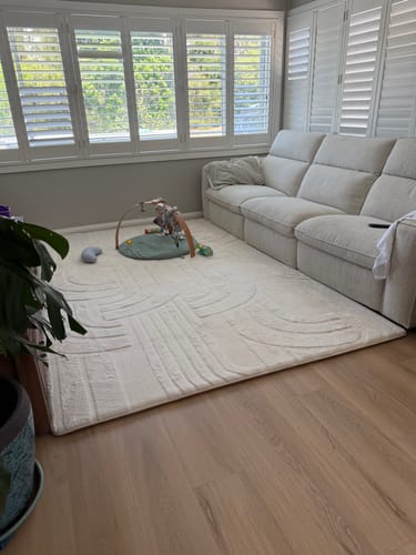 Customer's large cream Mellow Mat in a living room next to a sofa, with a baby play gym on top.