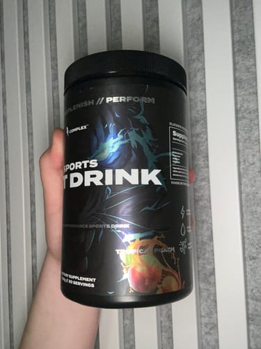 Customer holding the black tub of Sports Iont Drink, showing the Tropical Peach flavor label.
