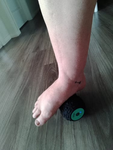 Customer rolling their foot over the black Vibit ROLL portable massage roller on a floor.