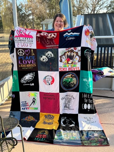 A happy customer holds up their large, colorful Premium T-Shirt Quilt, made from a patchwork of many shirts.