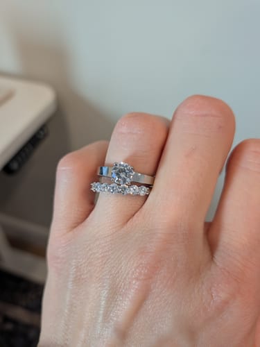 Customer's hand wearing the shiny Round Solitaire Engagement Ring paired with another sparkly band.
