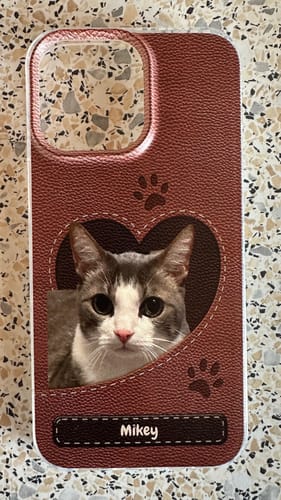 Kunde zeigt individuelle Handyhülle in brauner Lederoptik mit Katzenfoto in Herzform und dem Namen 'Mikey'.