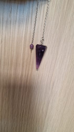 Photo d'un client montrant le pendule divinatoire en améthyste violette et sa chaîne argentée sur un fond en bois.