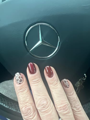 Kundin zeigt ihre UV-Gel-Nagelfolien in Dunkelrot mit Akzentnägeln im Leopardenmuster.