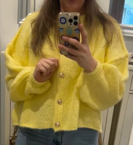 Kundin trägt den bequemen, gelben Cardigan 'CozyGlam' mit großen goldenen Knöpfen.