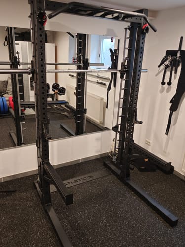 Rezensent zeigt das schwarze R7 Saber Squat Rack mit Multipresse, das in einem Home-Gym aufgestellt ist.
