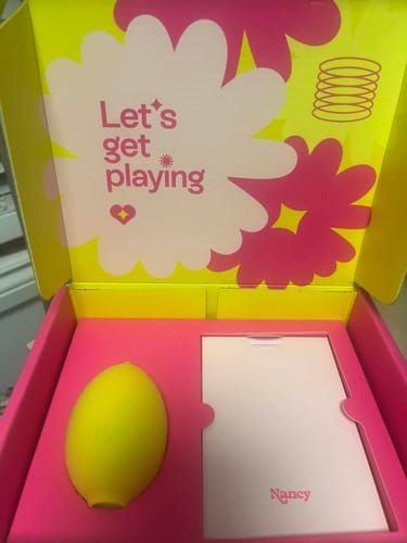 Reviewer unboxing their yellow Lem Clitoral Massager from its colorful pink and yellow box.