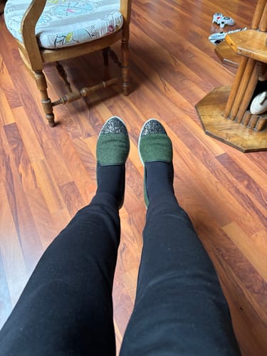 Une cliente portant les chaussons Bruson verts et pailletés, vus de dessus sur un sol en bois.