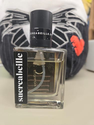 Customer's square glass bottle of Sansa perfume, showing the pale yellow liquid and black cap against a blurred background.