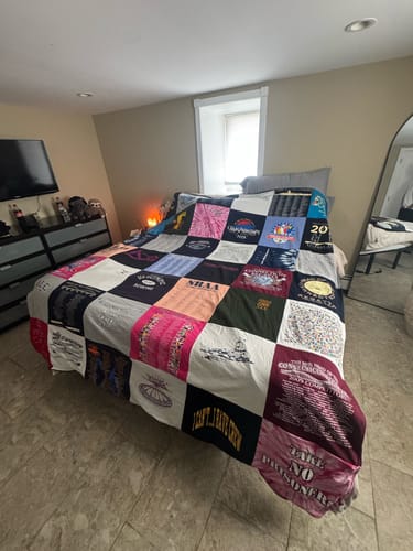 Customer's large Premium T Shirt Quilt, made of many colorful t-shirt squares, neatly spread across a bed.