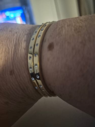 Close-up of a customer wearing two gold Eternity Bangle Slim bracelets stacked on their wrist.