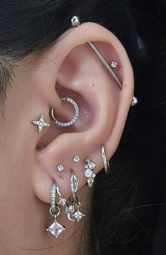 Reviewer's ear showing the silver Eclipsa Illusion Huggies with a dangling charm, styled with several other earrings.