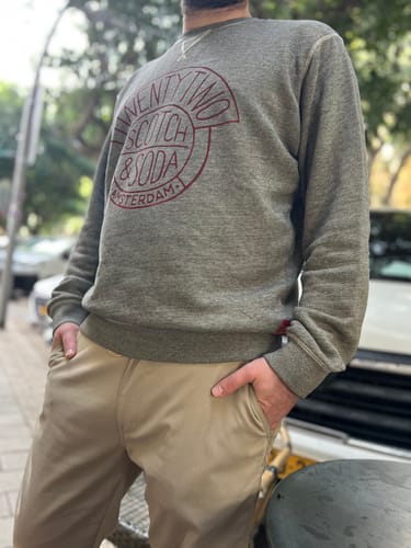 לקוח לובש את סווטשירט הגברים האפור עם הדפס אדום, עומד בחוץ.