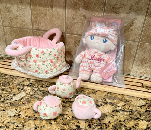 Customer's personalized Pudding Baby Girl doll with a matching fabric basket and plush tea set on a counter.