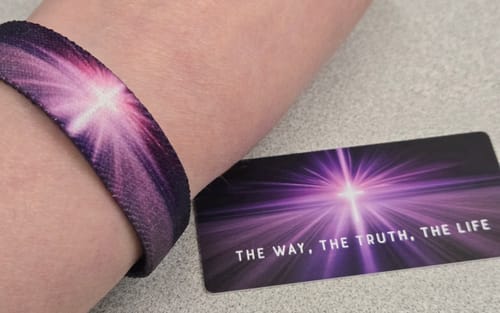 Reviewer's wrist wearing the purple 'The Way, The Truth, The Life' bracelet from the Gospel Bible Pack, next to its matching card.