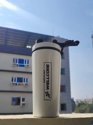 Customer's white Wellcore steel shaker with a black lid, resting on a balcony ledge against a blue sky.