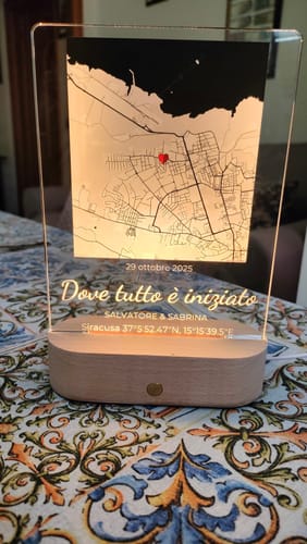 Ein Kunde zeigt das personalisierte Nachtlicht 'Dove tutto è iniziato', das auf einem Holzsockel steht und eine Karte beleuchtet.