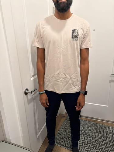 Customer wearing the TWO THUMBS UP TEE, showing the front view and regular fit in a hallway.