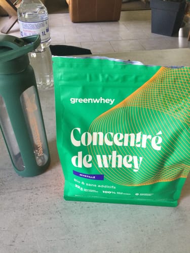 Sachet de Protéine de Whey Bioproduct d'un client, saveur myrtille, posé sur une table à côté d'un shaker.