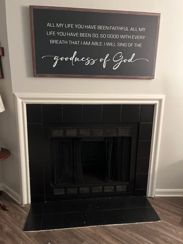 Reviewer's black Goodness Of God Faith Sign II hanging on a wall above their fireplace.