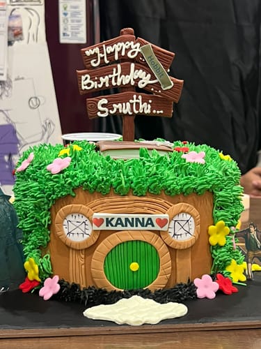 Customer's LOTR Theme Hobbit Cake designed as a hobbit house with green icing and a personalized 'Happy Birthday Sruthi' sign on top.