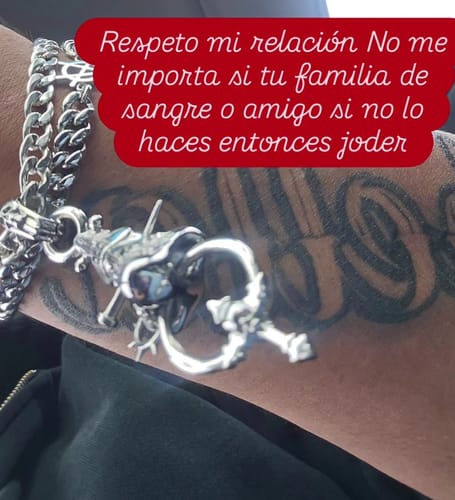 Close-up of a customer's silver-colored chain bracelet with a detailed charm, worn on their arm over a tattoo.