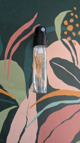 Reviewer's sample vial of Honeyberry perfume against a colorful, patterned background.
