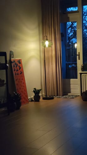 Recensent toont de Denise vloerlamp met groene glazen kap, die aan staat in de hoek van een kamer.