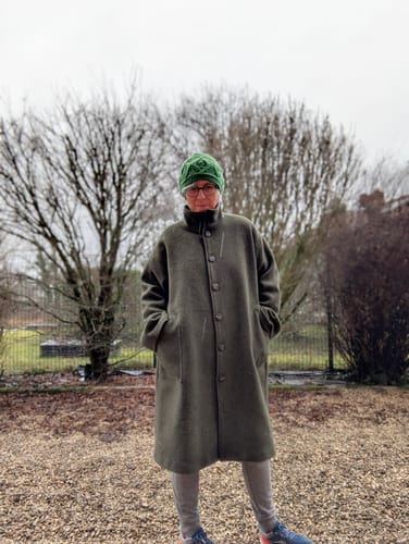 Cliente portant le Manteau Arthur vert, montrant sa coupe longue et ample.
