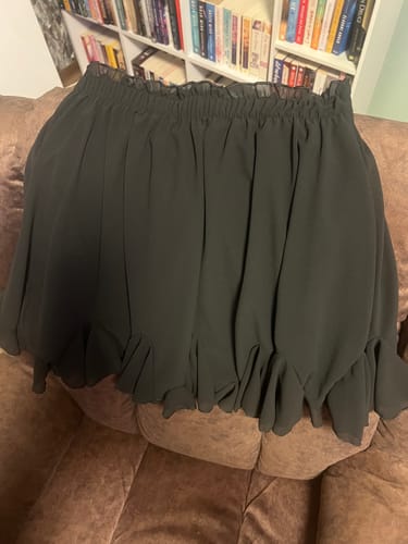 Ein Kunde zeigt den schwarzen Rock "Summer" mit hohem Volantbund, der auf einem Sofa liegt.