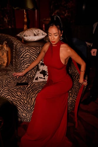 Reviewer posing in the red Naked Halter Maxi Dress on a couch, showing the halter top and long, flowing skirt.