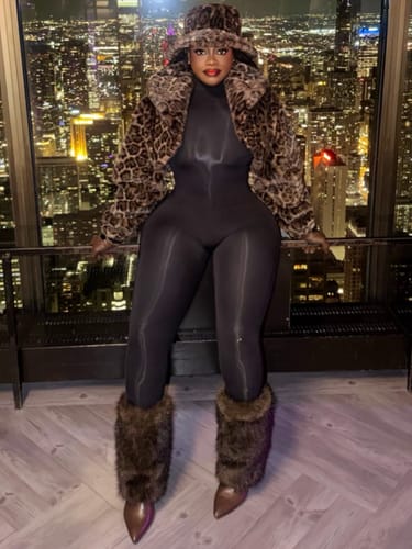 Reviewer in a black catsuit and leopard print coat, posing against a city skyline at night.