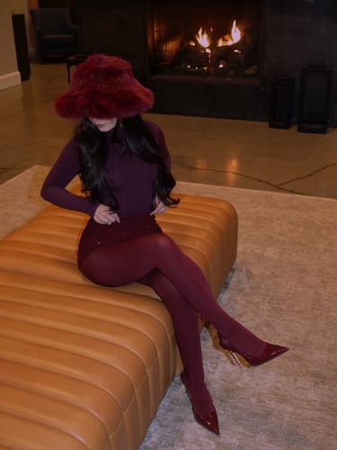 Reviewer seated indoors wearing a dramatic, red Faux Fur Oversized Bucket Hat with a matching outfit.