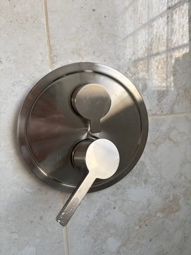 Close-up of a customer's brushed nickel dual-handle shower valve installed on a light-colored tiled wall.