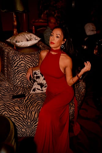 Reviewer sitting on a couch in the red Naked Halter Maxi Dress, showing a side view of the fitted silhouette.