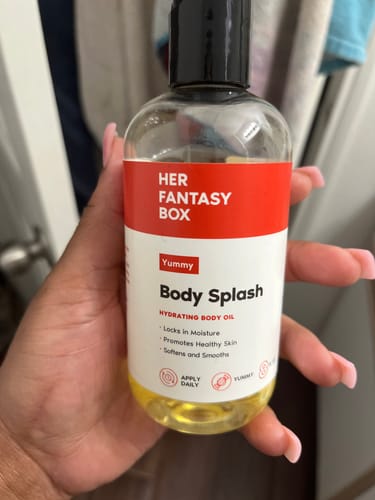 Customer holding the clear bottle of Yummy Body Splash hydrating body oil.