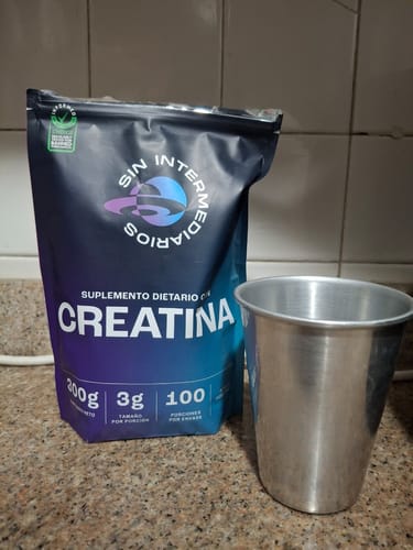 El envase de Creatina Monohidrato de un cliente sobre un mesón de cocina, al lado de un vaso metálico.