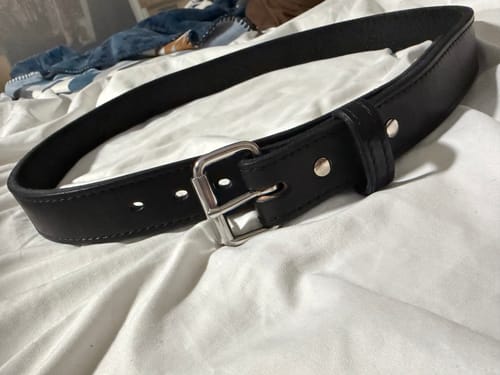 Customer's black leather Xtreme belt with a silver buckle, showing its decorative stitching, lying on a white surface.
