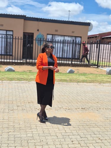 Reviewer standing outdoors wearing the classy Miss Black Lola 1 Court heels with a black dress and orange blazer.