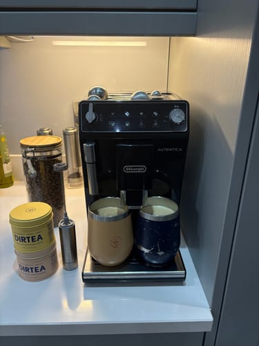 Reviewer's tins of Lion's Mane Mushroom Powder stacked on a counter beside a coffee machine preparing two drinks.